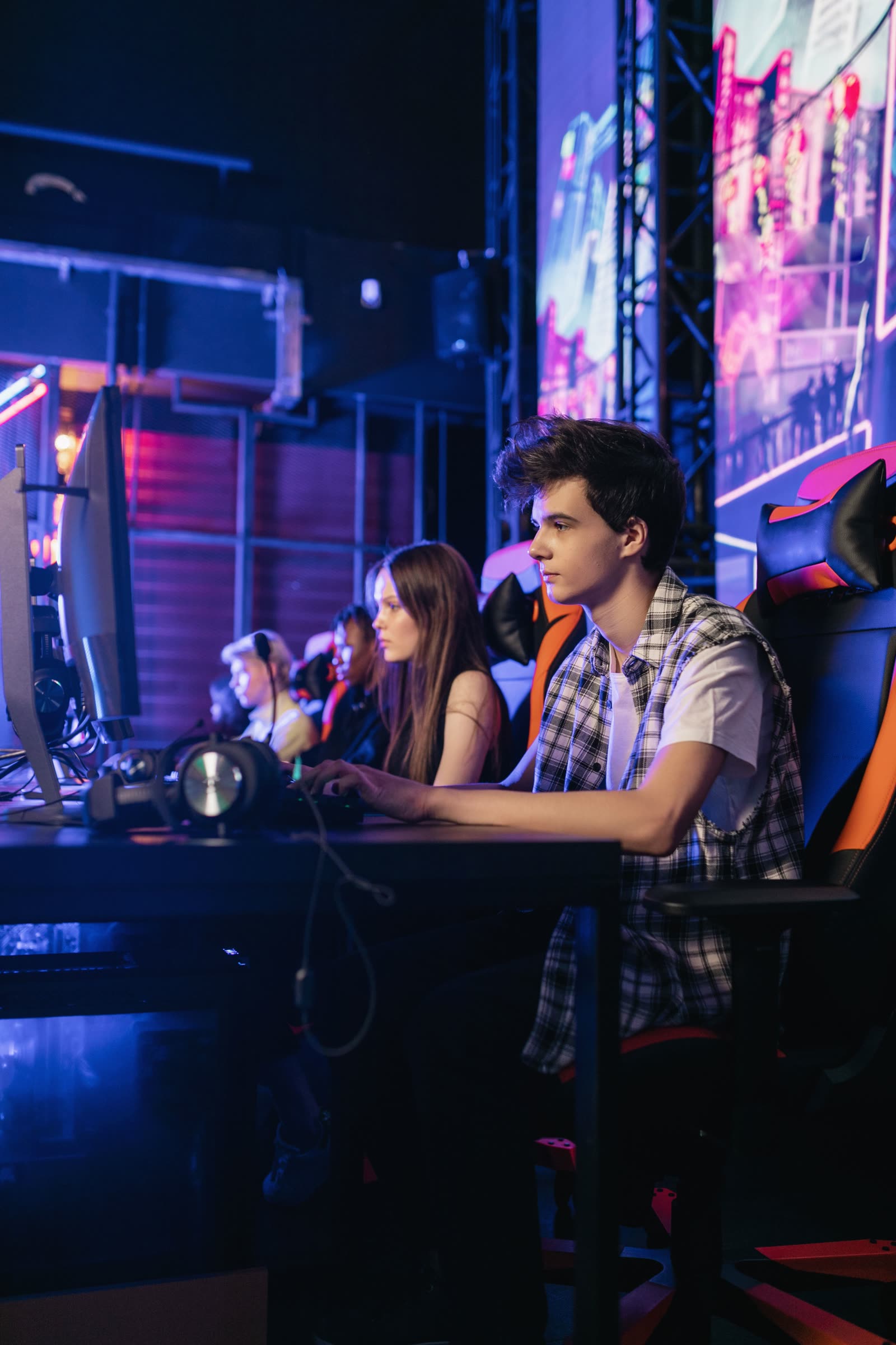 A long side-on row of gaming desks with screens and chairs receding down the hall