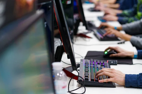 Hands typing on lit mechanical keyboards down a bright desk of monitors