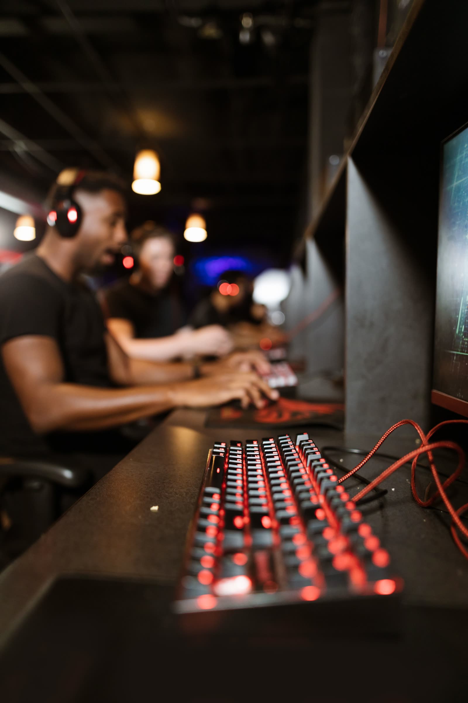 Player in headphones seated down a row of stations, a lit mechanical keyboard in the foreground