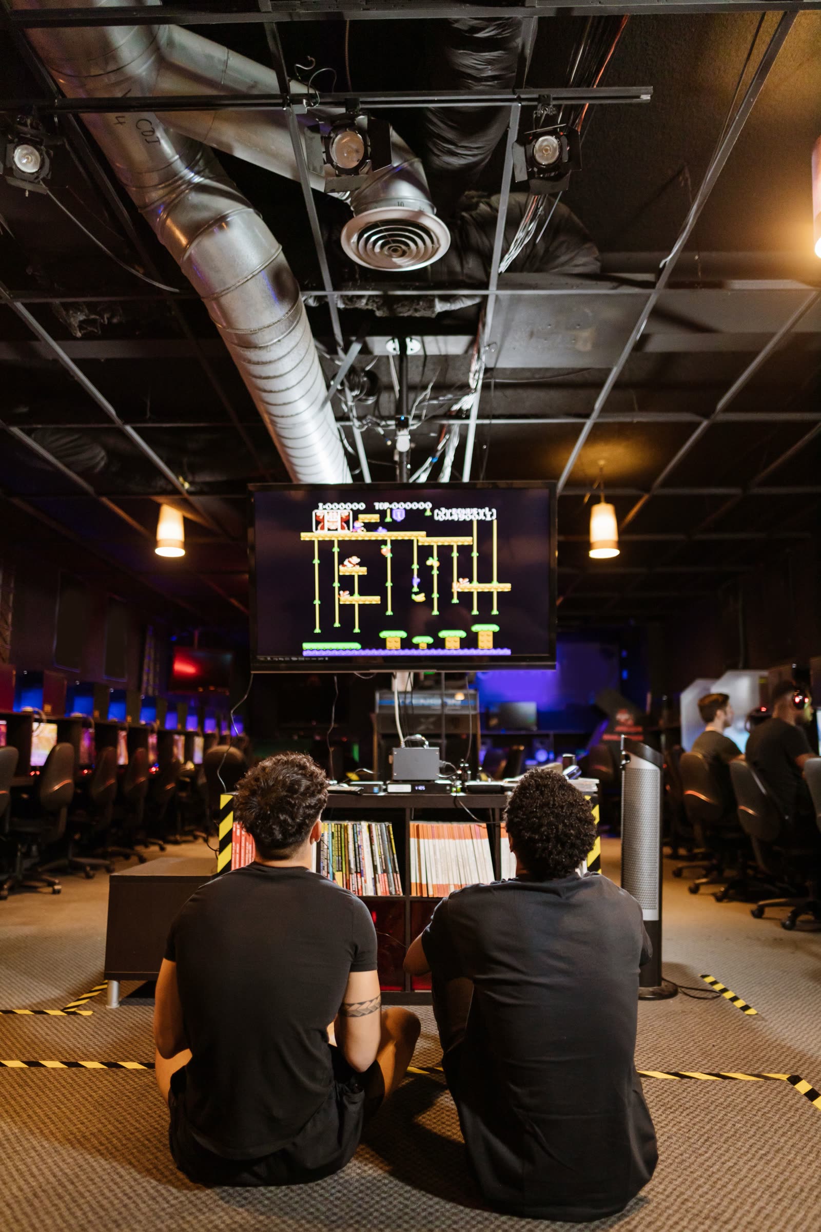Two players seated before a bright screen mounted above a low shelf of books